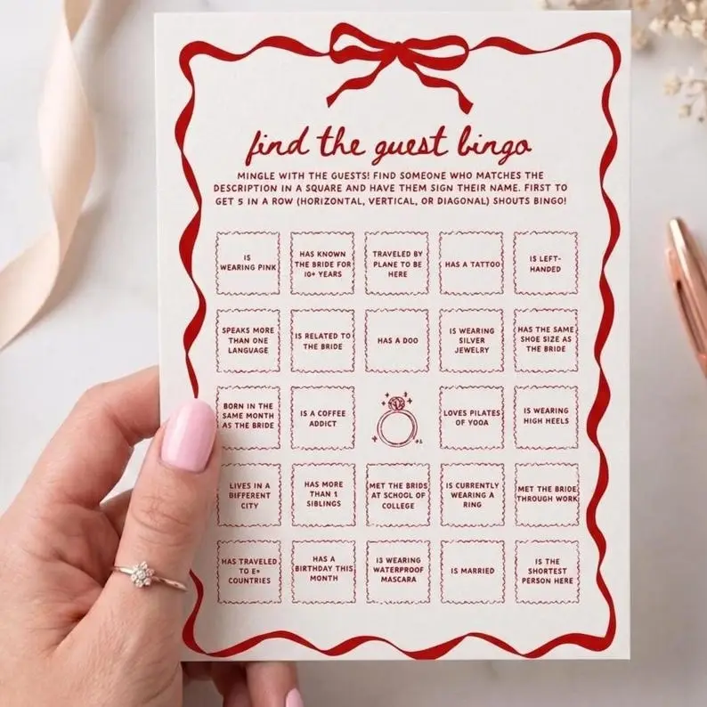 Find the Guest Bingo card on cream with a red wavy ribbon border tied in a bow, holding a five-by-five grid of scalloped squares with an engagement ring drawn in the centre