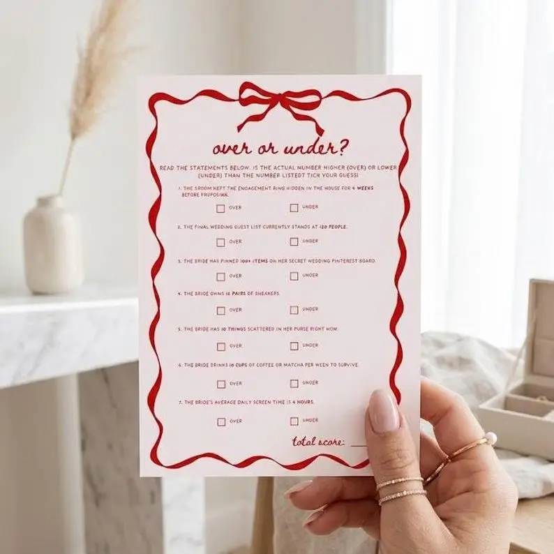 Over or Under game card in blush pink with a red wavy ribbon border and bow, listing seven statements about the bride each with an over and under tick box