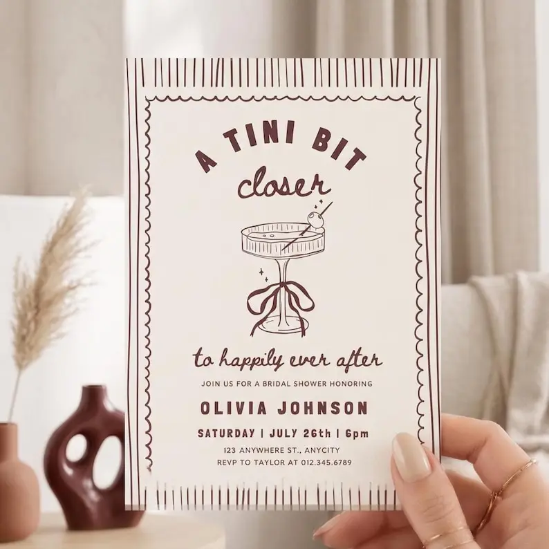 Tini Bit Closer bridal shower invitation in cream and burgundy with a hand-drawn wavy border and a coupe glass topped with an olive and a ribbon at the stem, shown as a single card
