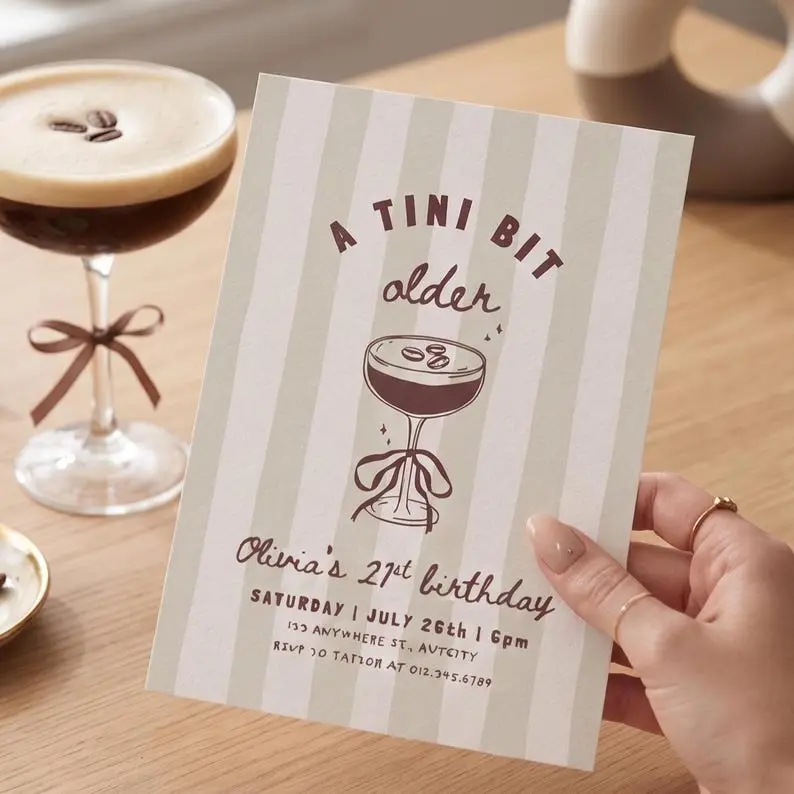 A Tini Bit Older birthday invitation on a greige and cream striped card in cocoa ink, with a hand-drawn espresso martini coupe finished with a bow