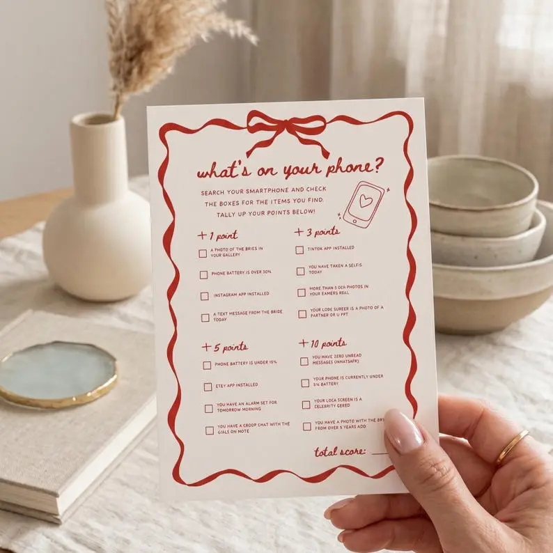 What's On Your Phone game card on cream with a red wavy ribbon border and bow, showing a drawn phone with a heart and items to find grouped into one, three, five and ten point tiers