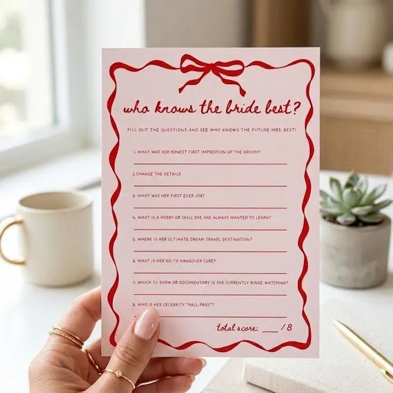 Who Knows The Bride Best game card in blush pink with a red wavy ribbon border and bow, holding eight written questions on ruled lines with a score box at the foot
