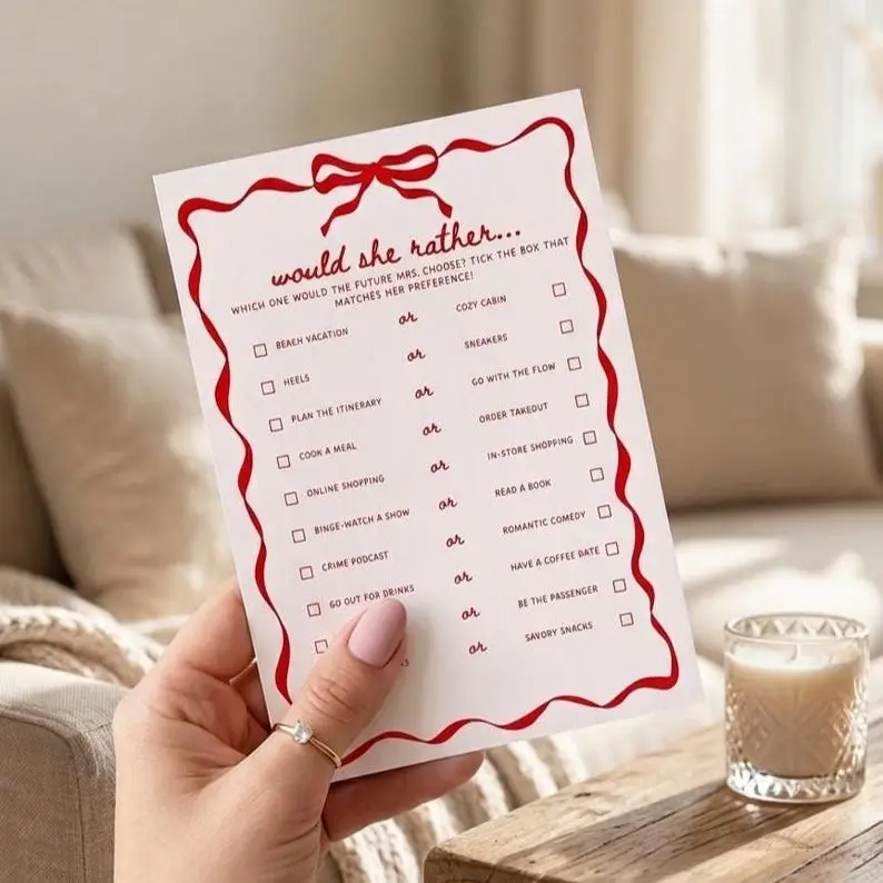 Would She Rather game card in blush with a red wavy ribbon border and bow, showing paired options in two columns separated by a script or, each with a tick box
